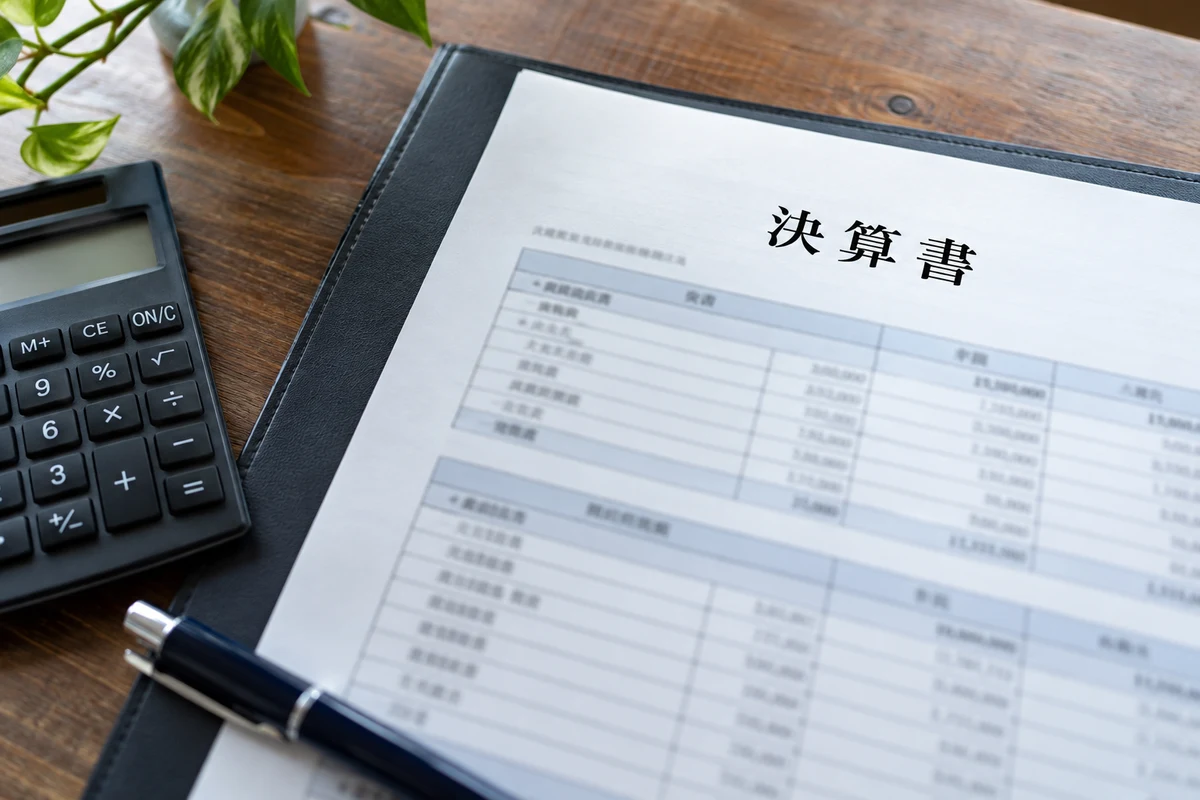 Báo cáo quyết toán 決算書 cùng máy tính cầm tay trên bàn làm việc.